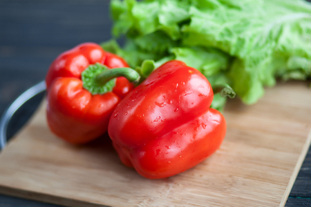 Vegetables lie on a chopping wooden board on a roustic table - salad and red sweet pepper. Close up photoの写真素材