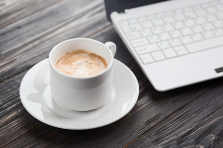 Coffee cup and laptop on the wood texture, selective focus on  cup of coffeeの写真素材