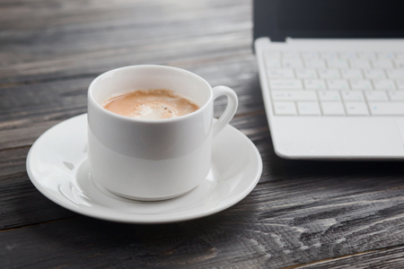 Coffee cup and laptop on the wood texture, selective focus on coffee cream.の写真素材
