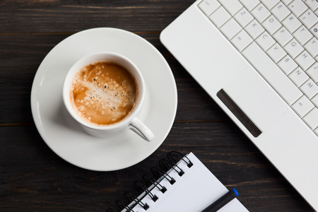 Office items with coffee cup, laptop and notepad on dark rustic wooden backgroundの写真素材