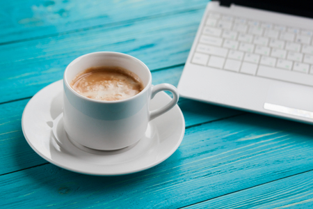 Office items with cup of coffee and laptop on a blue turquoise table. Selective focus on coffee cupの写真素材