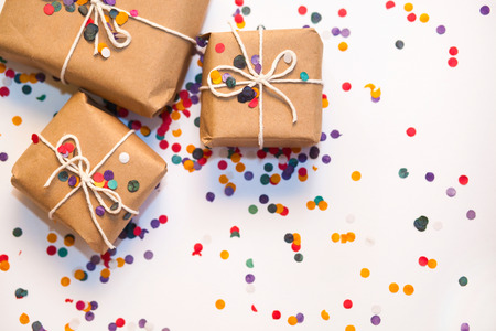 Present box with white bow on white background with multicolored confetti. Flat lay style. Christmas and new year conceptの写真素材