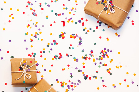 Present box with white bow on white background with multicolored confetti. Flat lay style. Christmas and new year conceptの写真素材