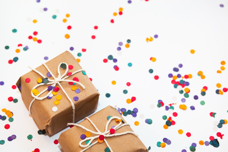 Present box with white bow on white background with multicolored confetti. Flat lay style. Christmas and new year conceptの写真素材