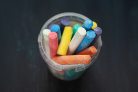 Black old empty chalkboard  with colorful pieces of chalk in plastic bucket.の写真素材