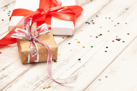 One brown gift box and two white paper boxes with red ribbon on white wooden board background with space for text.の写真素材
