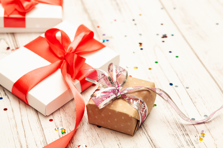 One brown gift box and two white paper boxes with red ribbon on white wooden board background with space for text.の写真素材
