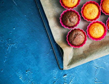 Delicious chocolate and vanilla cupcakes cooked in red tins on baking tray with baking paper on concrete table, top view.の写真素材