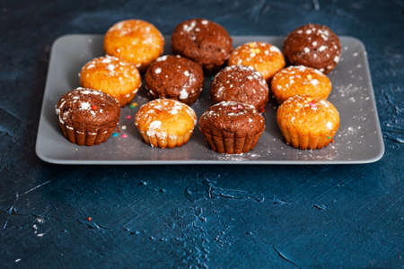 Delicious chocolate and vanilla cupcakes with sweet topping on textured concrete table, top view. Sweet pastries with powdered sugarの写真素材