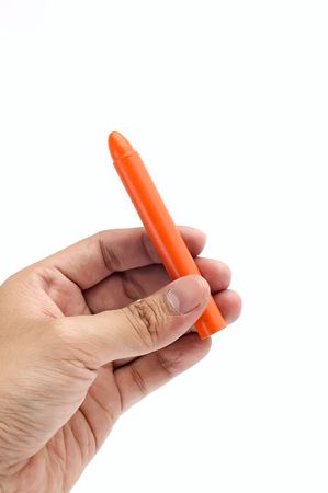 Hand holds orange crayon on white backgroundの写真素材