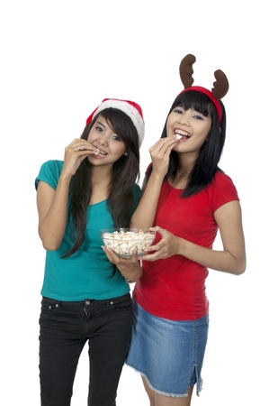 Two girls celebrate christmas and eat popcorn isolated over white backgroundの写真素材