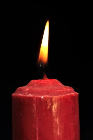 A single burning red candle isolated in front of black backgroundの写真素材