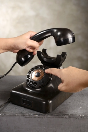 Human hand dialing numbers on antique telephone over abstract backgroundの写真素材
