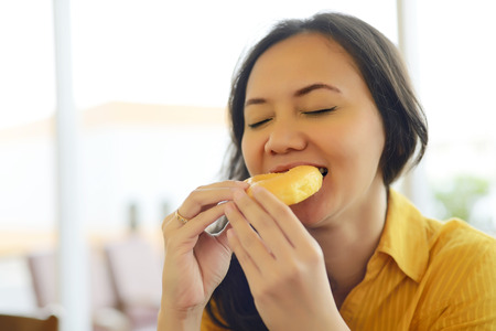Pretty Young Attractive Woman Eating Donut Enjoying Her Breakfast At Cafeの写真素材