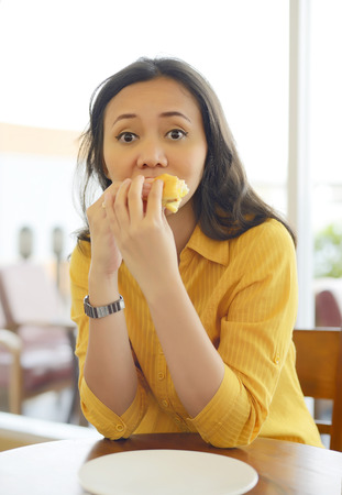 Pretty Young Woman Eating Burger Enjoying Break Lunch In Cafeの写真素材