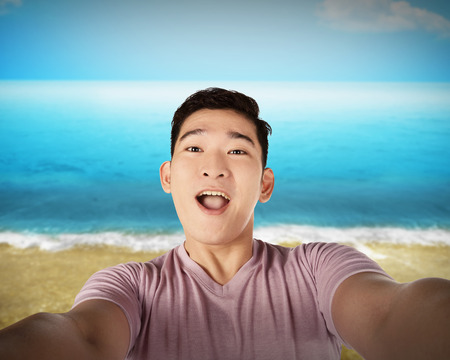 Handsome young man holding camera and making selfie on the beach. Vacation conceptの写真素材