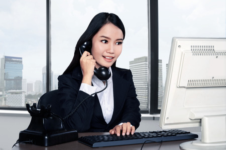 Smiling happy woman using computer with office backgroundの写真素材