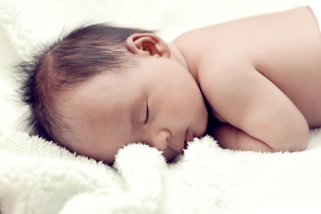 Peaceful baby lying on a bed while sleeping in a bright room over white sheetの写真素材