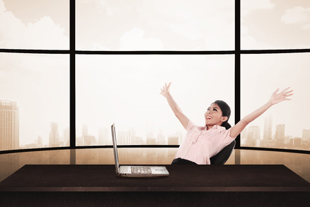 Business woman sitting on the chair with raise hand and laptop. Business success conceptの写真素材