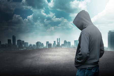Faceless man in hood on the rooftop with city backgroundの写真素材
