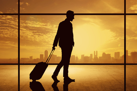 Silhouette of business man walking with suitcase over city background. Business travel conceptの写真素材