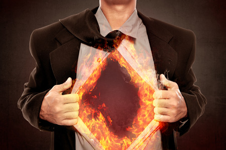 Business man tears open his shirt in a super hero fashion getting ready to save the day with fire around his shirtの写真素材