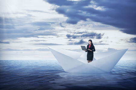 Asian business woman working with laptop on the paper boat, sailing on the seaの写真素材