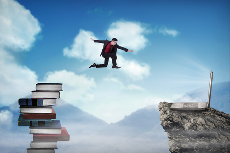 Concept of technology migration with business person jumping from book to laptopの写真素材