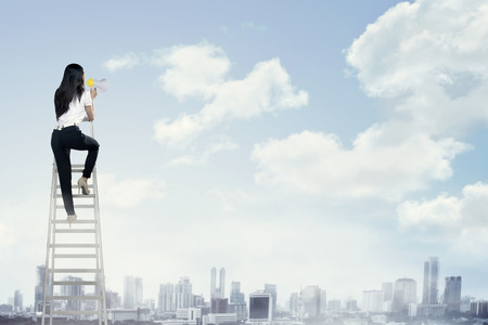 Business woman standing on the ladder high and shout with megaphone. Leadership conceptの写真素材