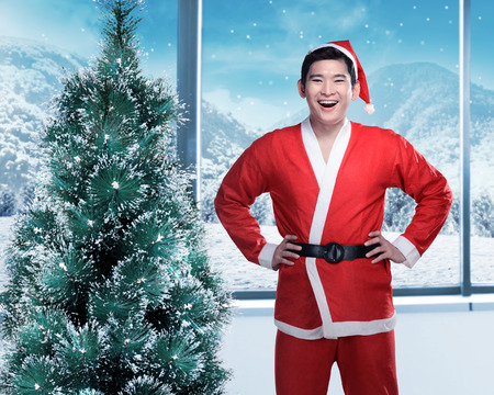 Asian man in santa claus costume standing near christmas treeの写真素材