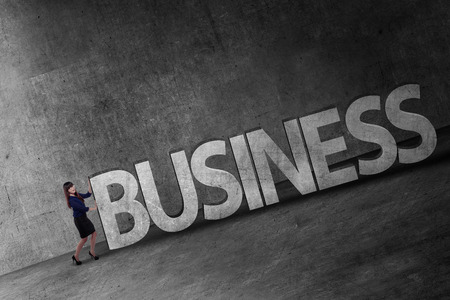 Asian business person pushing 3D business word uphillの写真素材