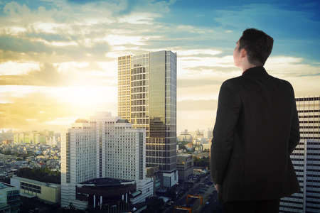 Back view of asian business man looking the sky on the building rooftopの写真素材