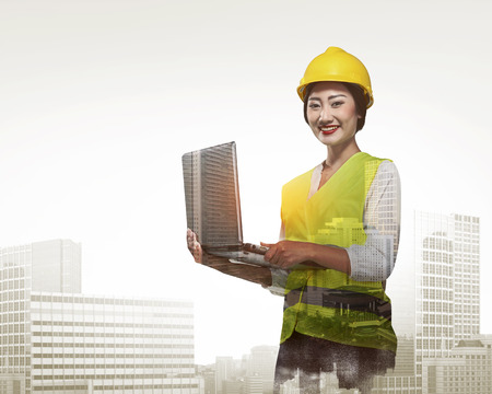 Double exposure of business woman in safety vest working with laptopの写真素材