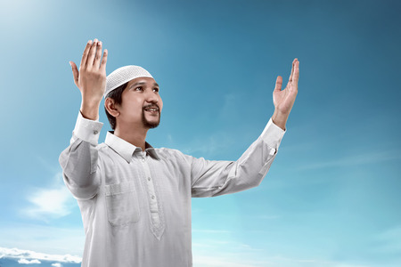 Young muslim man praying over blue sky backgroundの写真素材