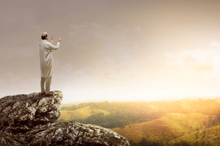 Image of muslim man standing on the top of cliff. Praying and looking to the skyの写真素材