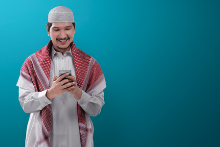 Young asian muslim man standing, wearing cap and holding the phoneの写真素材