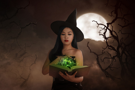 Asian wizard woman holding spell book with moonlight backgroundの写真素材