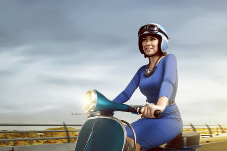 Asian woman riding a scooter in the afternoon wearing blue shirtの写真素材