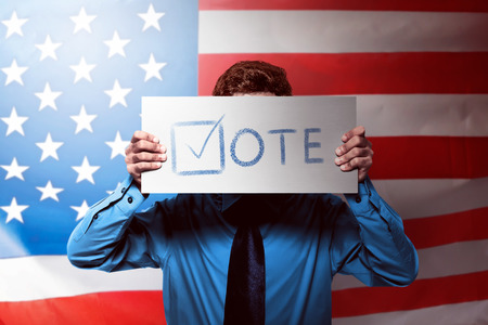 Young man with formal blue shirt holding a card with vote message textの写真素材