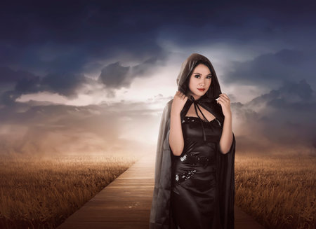 Beautiful asian witch woman with black hood on the meadowの写真素材