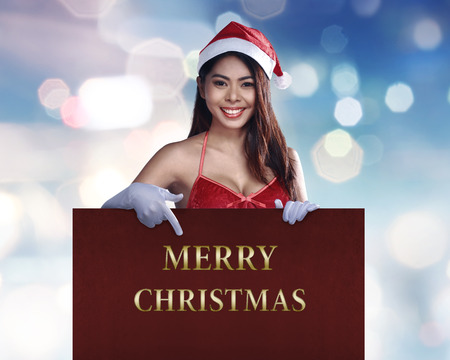Beauty asian woman in santa dress pointing Merry Christmas text in the signboardの写真素材
