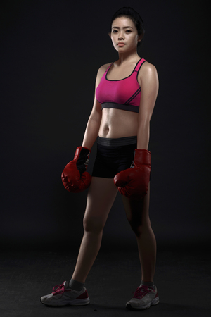 Beautiful asian woman boxer wearing red gloves posing over black backgroundの写真素材