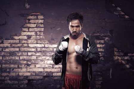 Strong asian boxer with strap in his hand waiting for fight against ruin brick wall backgroundの写真素材