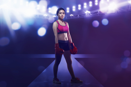 Smiling asian boxer woman with boxing glove standing in the stageの写真素材