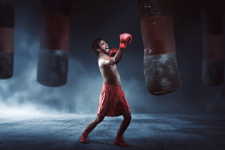 Asian male boxer practicing with a punching bag on dark roomの写真素材