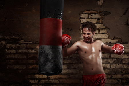 Asian male boxer practicing with a punching bag against ruin brick wall backgroundの写真素材