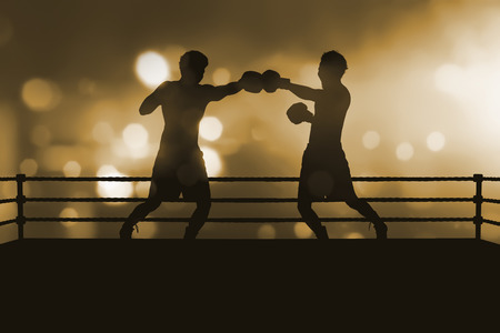 Silhouette of two professional asian boxer fight in the boxing match against blurred spotlightの写真素材