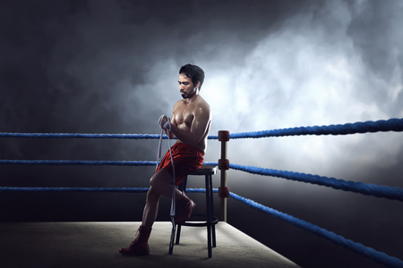 Sporty asian boxer man sitting on ring while wearing strap on wristの写真素材