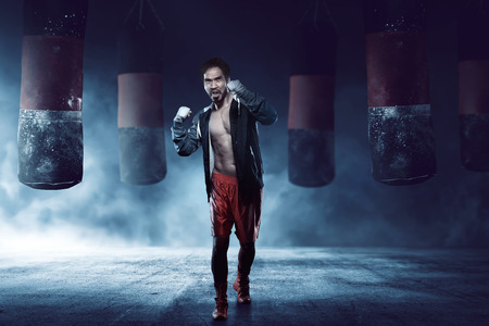 Muscular asian adult boxer man training against punching bag backgroundの写真素材