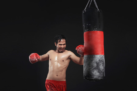 Muscular asian man boxer training with punching bag over black backgroundの写真素材